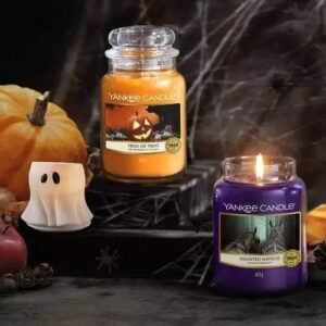 Yankee Candle Halloween Düfte, dekorativ dargestellt im Grusel Look mit Spinnenweben, im Detail Haunted Hayride und Trick Or Treat 623g, daneben auf der Linken Seite ein Votivkerzenhalter in Form eines Geistes